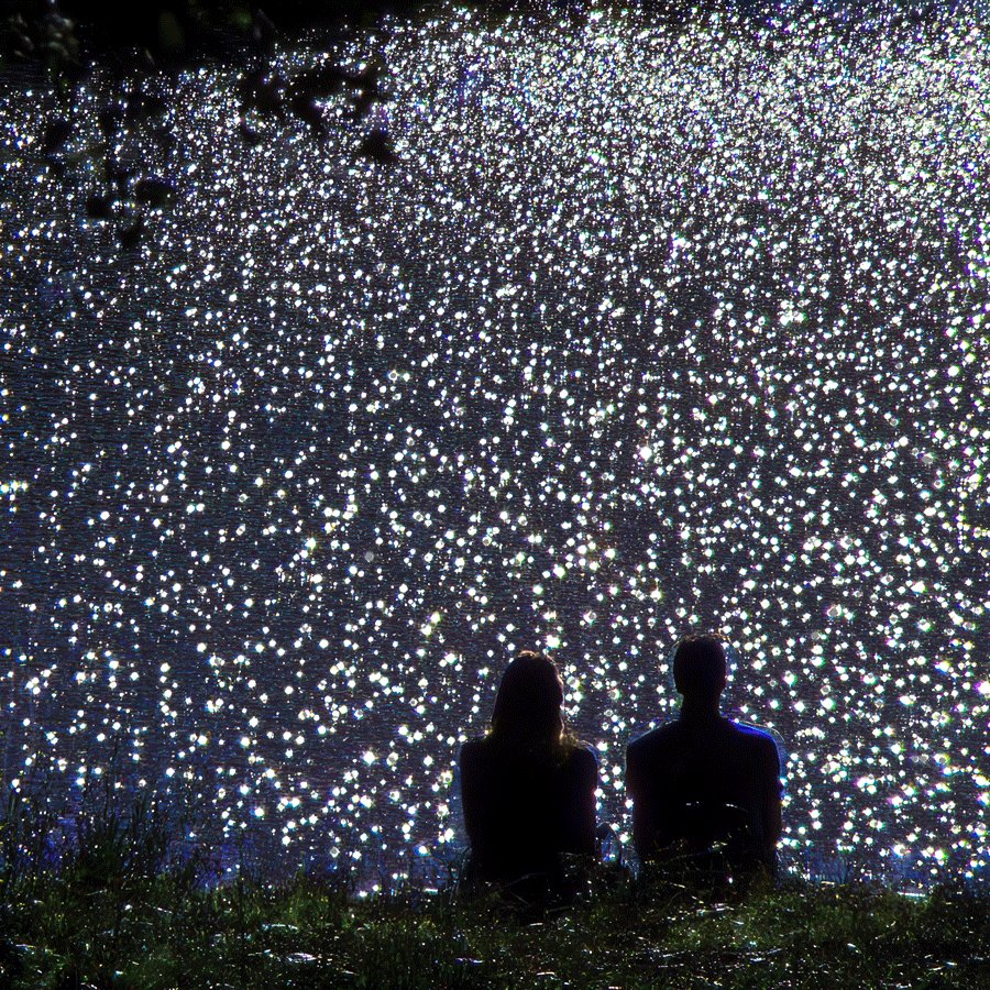 The image features two people sitting next to each other, possibly enjoying a beautiful night under the stars or watching a meteor shower. The sky above them is filled with numerous shooting stars, creating a captivating atmosphere for their experience. The photo captures the essence of the moment and adds an element of wonder to the scene.
