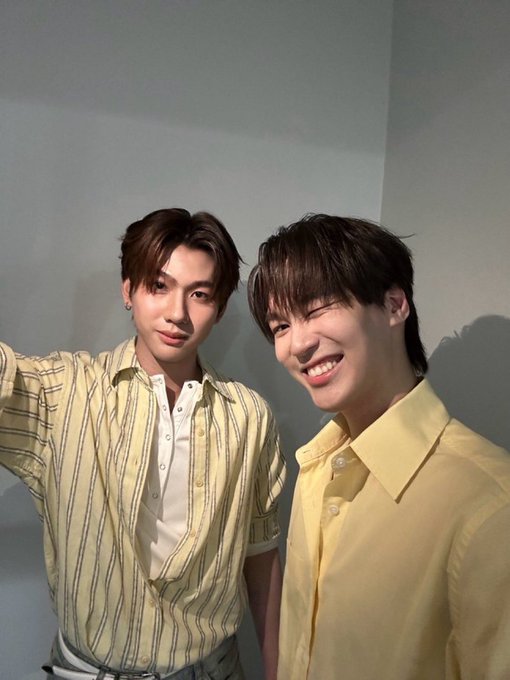 Two young men smiling in a selfie-style photo, one in a yellow striped shirt and the other in a solid yellow button-up shirt.