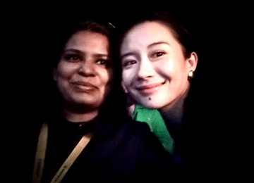 A dimly lit photo of two women smiling at the camera, one with short hair and one with longer dark hair.