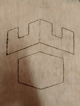 A hand-drawn design on light wood featuring a simple geometric emblem with a six-sided hexagonal shape outlined in dark pencil or pen. The post appears to be seeking feedback on this artwork as part of a contest submission for Romer and Gamdom, with the hopeful creator asking for opinions on their minimalist design.