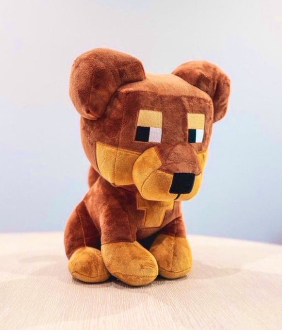 A plush toy of a pixelated brown dog sitting on a light-colored surface against a pale background.