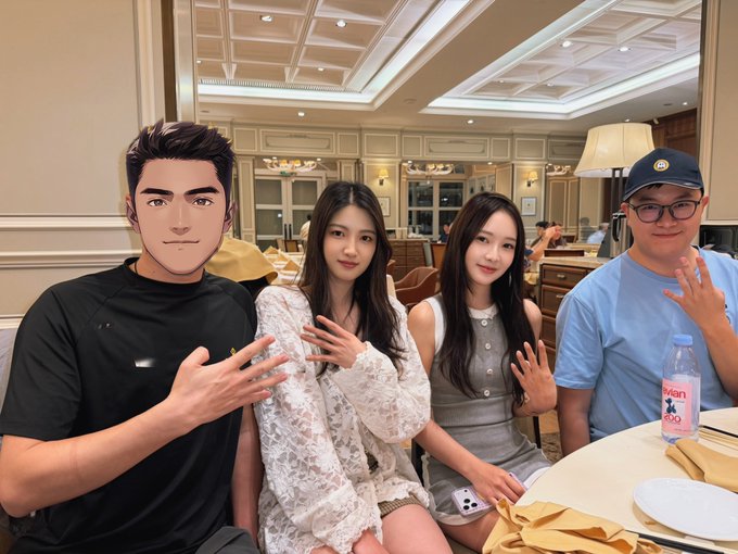 Four people pose for a photo at a restaurant table; one person's face is edited with a cartoon illustration, while the other three (two young women and a young man wearing a cap) smile and make hand gestures.