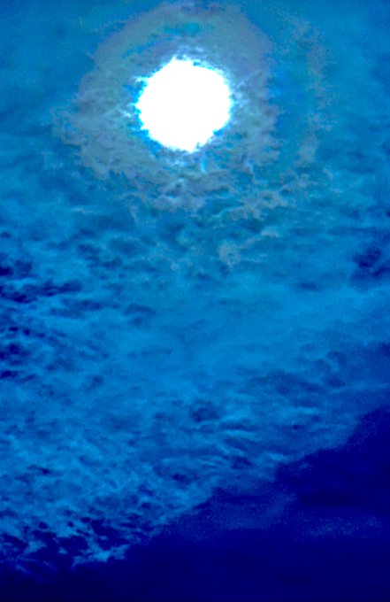 The sun shines brightly through clouds in a heavily blue-tinted, almost underwater-looking view of the sky.