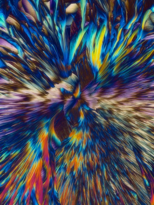 An abstract, psychedelic artwork featuring vibrant streaks of blue, yellow, red, and purple radiating outward in a swirling pattern.