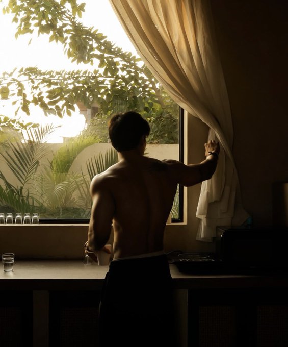 A shirtless man opens a curtain by a sunlit window, his back turned toward the camera. The warm, contemplative scene captures a quiet morning moment that reflects the post's sentiment of gratitude for a new day.