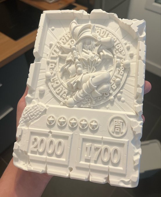 A white, 3D-printed collectible card featuring a central character illustration within a circular design, displaying "2000" and "1700" along with a Chinese character for armor, held in hand at the Card Expo at Bitcoin Asia.