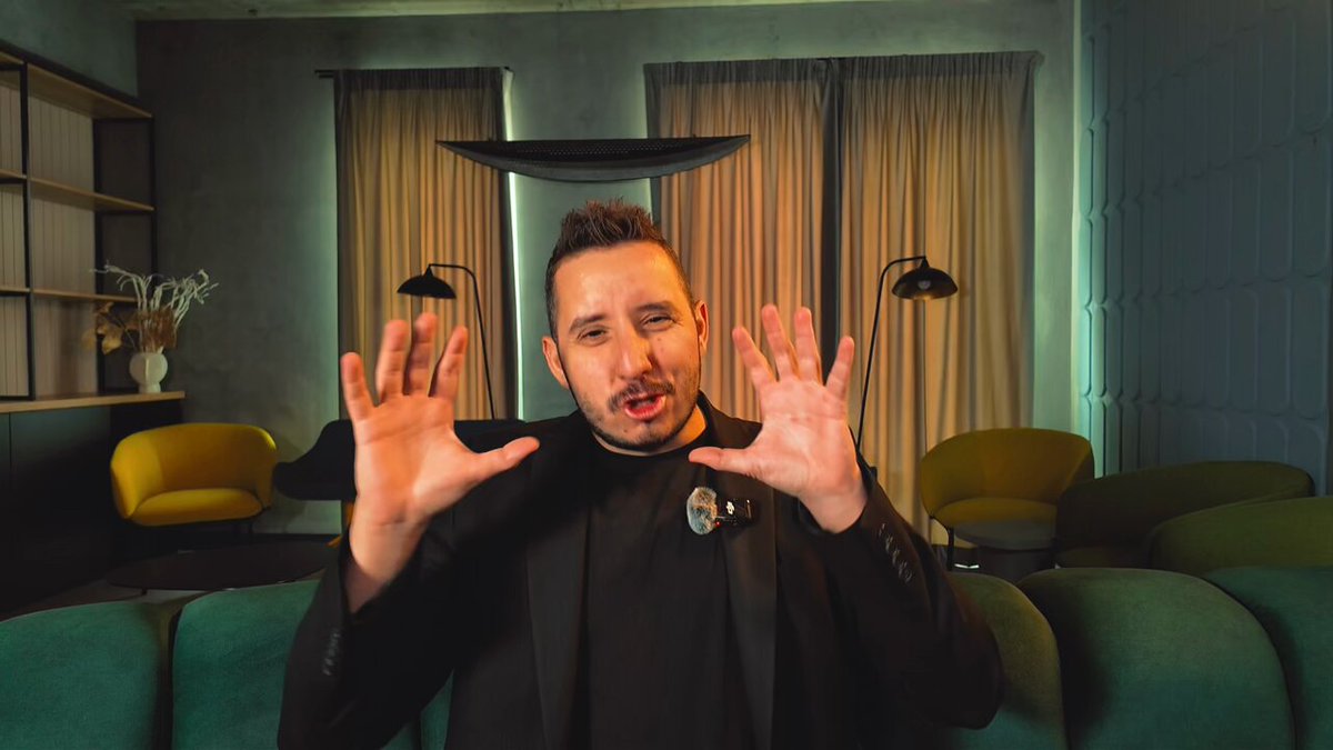 The image features a man wearing a black suit standing in front of a couch with his hands up in the air. The background includes a window with curtains and a lamp, creating an indoor setting. There are also two chairs visible in the scene. The image is related to a post that talks about transferring money or credit card information, suggesting that the man's actions might be connected to this transaction.