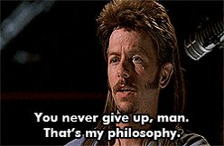 The image features an actor with a mohawk, wearing sunglasses, standing against a dark background. Below him, there's text that reads "You never give up, man. That's my philosophy." The actor appears to be looking off into the distance or at something in the distance while reading this message.
