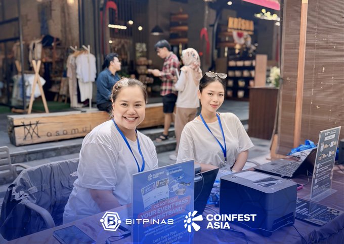 Two women smiling at a booth for 'BITPINAS' and 'COINFEST ASIA', with a sign reading 'DON'T MISS YOUR EVENT PASS AT BITBANK!'.