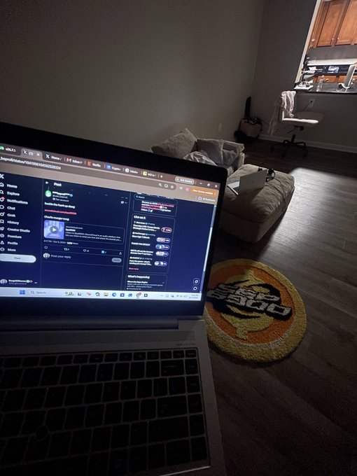 A laptop screen displaying a Discord server sits open in a dimly lit room, with a Doja Cat logo rug visible on the floor in the background.
