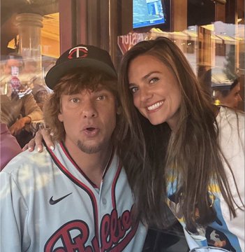 A man wearing a Minnesota Twins baseball jersey and cap poses with a smiling woman with long brown hair, taken at what appears to be a sports venue.