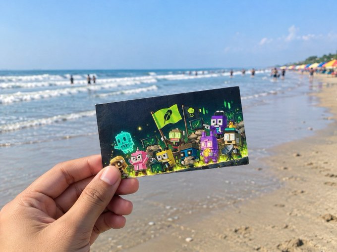 A hand holds up a postcard featuring colorful cartoon creatures with a green flag, set against a beach backdrop with ocean and people in the water.