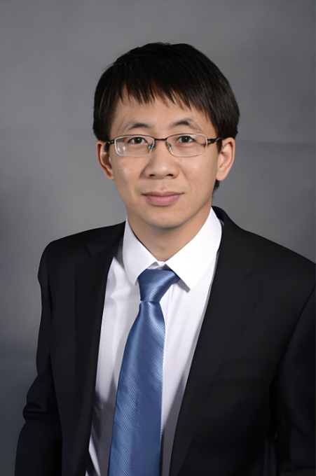 A professional headshot of an Asian man wearing glasses, a dark suit, a white shirt, and a blue tie against a gray background.