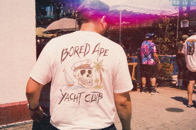 A man seen from behind wears a white t-shirt featuring a pirate skull design and the text "BORED APE YACHT CLUB," aligning with the post's "GM bored ape yacht club" greeting.