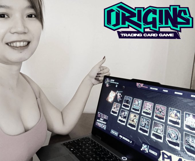A woman pointing at a laptop screen displaying the 'ORIGINS TRADING CARD GAME' interface, which shows a collection of digital character cards.
