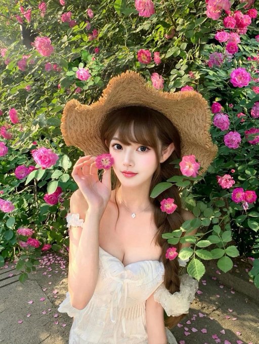A portrait of a young woman wearing a straw cowboy hat and white dress, posing among pink roses and greenery.
