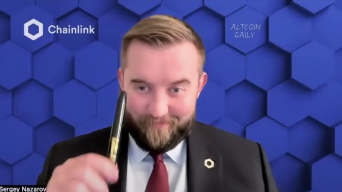 Sergey Nazarov, CEO of Chainlink, holds up a pen while appearing on "Altcoin Daily" against a blue hexagonal backdrop featuring the Chainlink logo. The image humorously suggests Nazarov is armed and ready to "exuberantly" defend Chainlink ($LINK) and the broader crypto market, including $BTC and $ETH, should regulatory clarity pass.