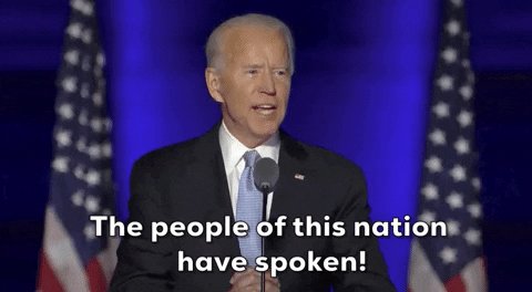The image features a man standing at a podium, wearing a suit and tie, with his hands placed behind him as he speaks into a microphone. In front of him are two American flags, one on each side of the stage. The text "THE PEOPLE OF THIS NATION HAVE SPEAKED!" is displayed above the man's head, indicating that he has just delivered a speech or addressed an audience.