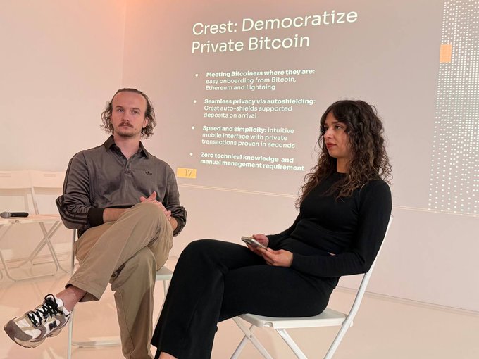 Two people sit on white chairs in front of a projection screen displaying a slide titled 'Crest: Democratize Private Bitcoin' with bullet points about meeting Bitcoiners, seamless privacy, speed, simplicity, and zero technical knowledge required.