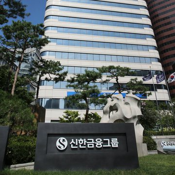 The image shows the Shinhan Financial Group building with a stone sign reading "신한금융그룹" (Shinhan Financial Group) and an "S" logo, set against a backdrop of the bank's modern glass-and-steel headquarters. This visual ties directly to the news that Shinhan Bank has successfully completed a stablecoin pilot for corporate overseas remittances, with technical support from the Solana Foundation—highlighting the institution behind the innovative blockchain-based financial initiative.