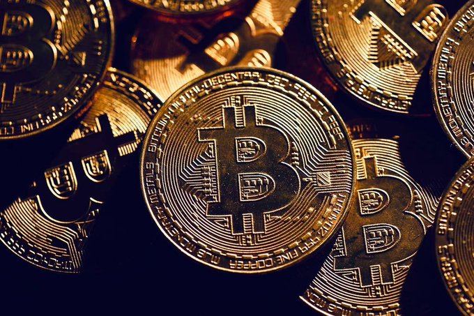 A close-up photograph of multiple gold-colored Bitcoin coins stacked together.