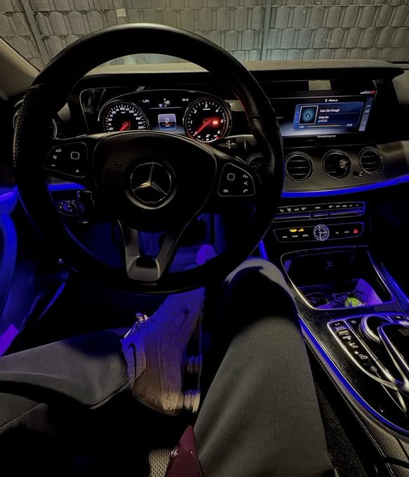 A first-person view from the driver's seat of a Mercedes-Benz at night, with the dashboard illuminated, showing an infotainment screen displaying "Don't Get Caught" and "Classic Hits" radio, paired with the ops' promotion offering breakfast for $50 max per person.