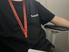 A person wearing a black "Switch" branded t-shirt and a red lanyard sits in an office chair, embodying the casual work setting described in the post where the "wear-to-earn" concept is integrated into everyday office life, including during an in-house lecture. The relaxed posture and work attire visually reinforce the theme of seamlessly blending daily routines with Web3 culture.
