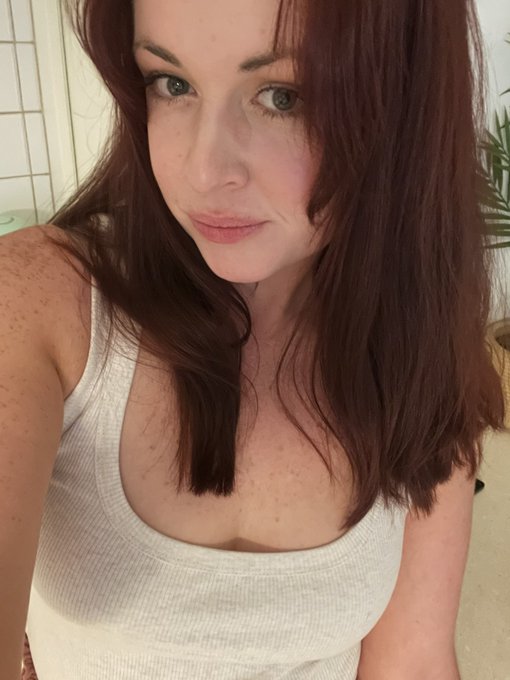 A selfie of a woman with long auburn hair wearing a light gray ribbed tank top.