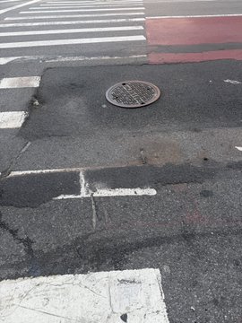 A cracked New York City sidewalk with a manhole cover sits beside a crosswalk, reflecting the aftermath of a fall on the unforgiving pavement. The image underscores the poster's resilience, as they got back up driven by their investment in $ANSEM.