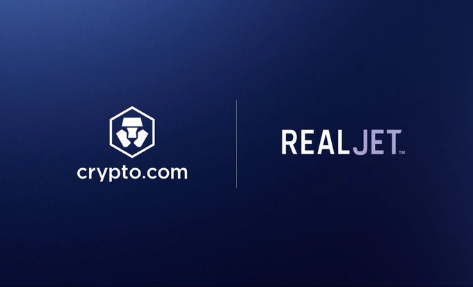 The image features a dark blue gradient background displaying the Crypto.com logo on the left and the "REALJET" brand on the right, separated by a vertical line. The graphic visually represents the partnership between the two companies, highlighting REAL Jet as the first private aviation company to integrate Crypto.com Pay into its charter booking platform.