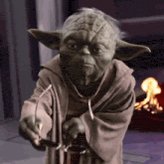 In the image, a Yoda character from Star Wars holding glasses is positioned against a backdrop of a fire with flames in the background. The scene also contains some text that reads "ALGO to $0.50+? It's not a prediction,it's the prophecy. Yoda approves: "#ALGO #Algorand #Crypto #Blockchain #Web3 #DeFi #Altcoins #BullRun #HODL" which suggests there is some sort of relation between the glasses and the ALGO or some form of prophecy involving Algo technology. The text might be a part of a story, description, or message associated with the image.