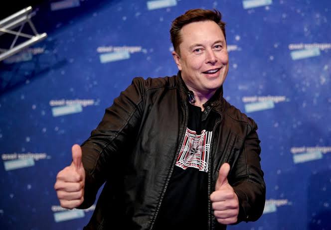 Elon Musk gives a double thumbs-up in a black t-shirt with a red graphic design, standing in front of a blue backdrop. The image accompanies a post claiming that his platform X is enabling Bitcoin purchases, suggesting his approval of the cryptocurrency integration.