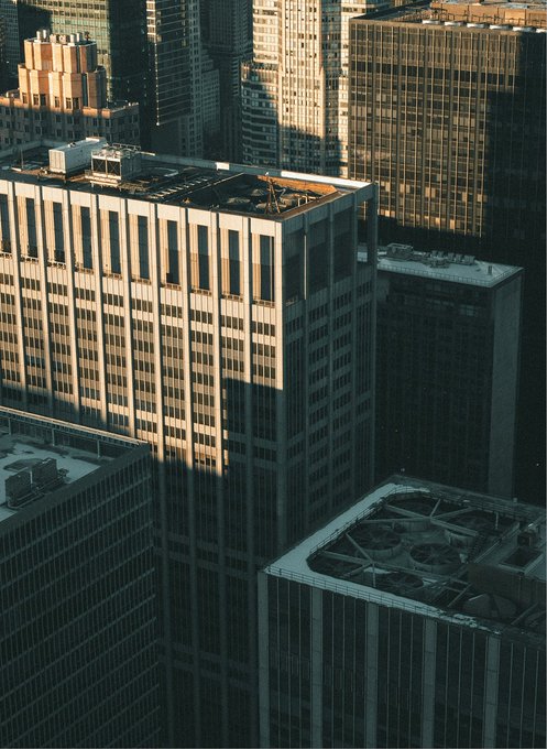 An aerial view of densely packed urban skyscrapers bathed in warm sunlight and deep shadow. The cityscape metaphorically represents the regulatory framework of the SEC's new "Regulation Crypto Assets," symbolizing how the structured "city" of financial regulations provides clear pathways (registration exemptions up to $5 million over four years or $75 million annually) amid the complex, towering landscape of crypto investment contracts.