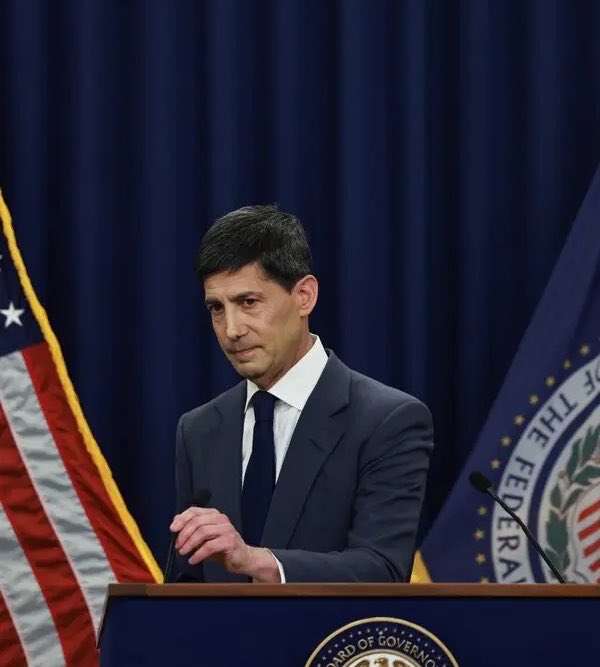 A man in a dark suit stands at a podium with the partial text "BOARD OF GOVERN..." visible, flanked by the American flag and a seal reading "...OF THE FEDERA...", appearing to address the press amid news that US CPI came in at 3.4% as expected, causing BTC to briefly dip to $76K before bouncing back.