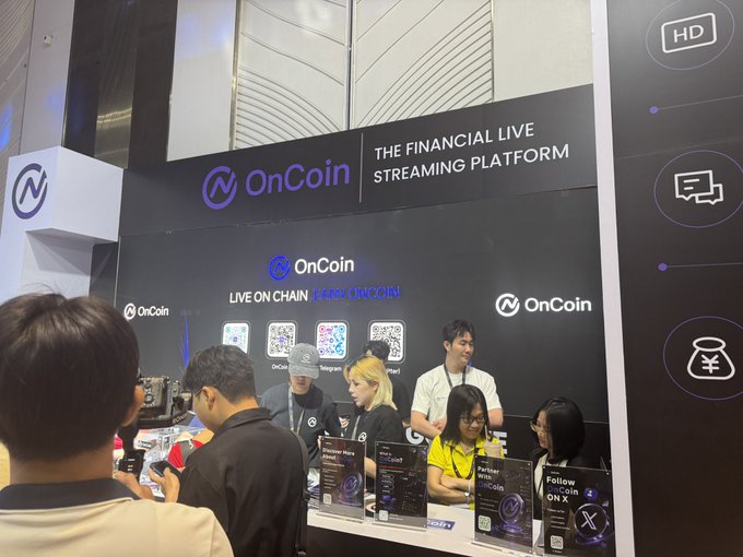 A crowded OnCoin booth at the Conviction event, with staff and attendees gathered around a counter displaying merchandise and QR codes. Visible signage reads "OnCoin - THE FINANCIAL LIVE STREAMING PLATFORM" and "LIVE ON CHAIN @ARE_ONCOIN," aligning with the post's mention of an Early Bird Badge for accumulating airdrop points.