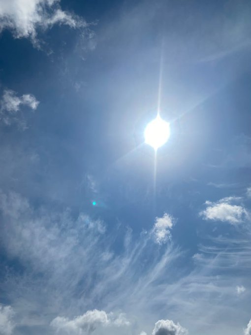 A bright sun shines in a blue sky with scattered white clouds and wispy cirrus formations.