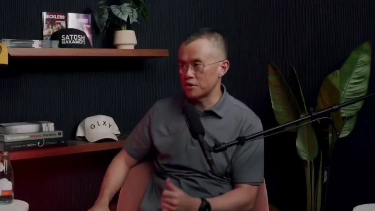 The image shows a man sitting at a desk with a microphone, wearing glasses and holding a microphone. The background features a bookshelf filled with various items such as books and potted plants. There are also several books scattered around the room. A caption on the image reads "CZ Binance proposes a controversial timeline to freeze Satoshi's 1 million Bitcoin before a quantum hack happens." This suggests that there is an ongoing discussion or debate about the value of Bitcoin, with some people advocating for freezing it as a precautionary measure against potential threats like quantum hacking.

The man sitting at the desk appears to be engaged in this conversation, possibly discussing the implications and risks associated with Bitcoin's current value and its future trajectory. The presence of books on the shelf indicates that there might be additional resources or information available for those interested in learning more about Bitcoin and its potential impact on society.