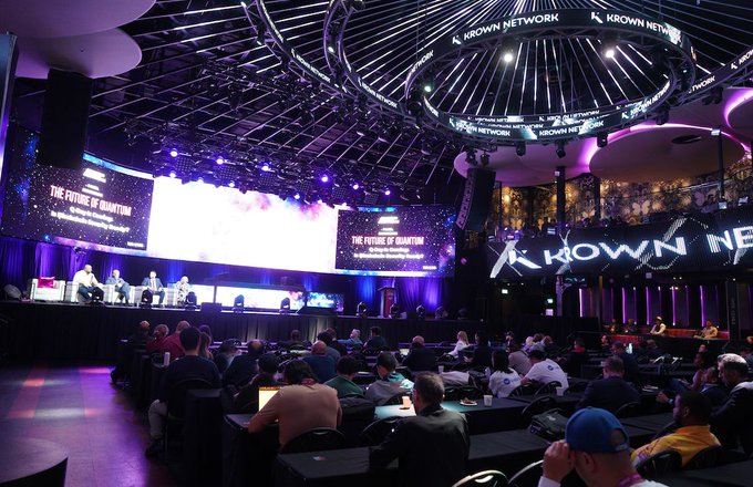 A conference event with panelists on stage at the 'Krown Network' venue, with screens displaying 'THE FUTURE OF QUANTIME' to the seated audience.