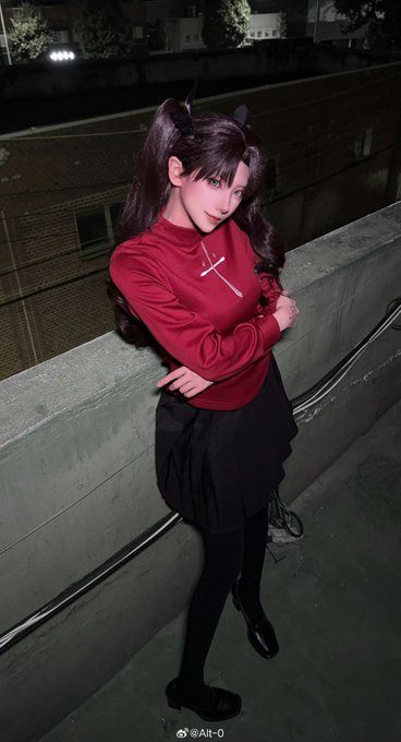 A cosplayer portraying Rin Tohsaka from Fate/stay night stands on a rooftop at night, wearing her signature red top, black skirt, and twin-tails hairstyle. The watermark "Alt-0" appears at the bottom, matching the poster's username, suggesting this is a cosplay photo shared by that user.