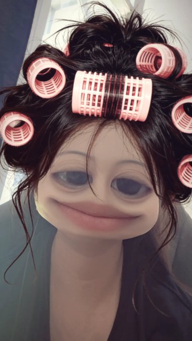 A woman wears pink hair rollers and a digitally distorted filter that exaggerates her smile and eyes, creating a surreal, cartoonish appearance.