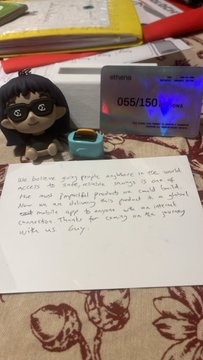 A handwritten message expressing the company's mission to provide global access to safe mobile savings, displayed alongside a small figurine, a smart meter showing "055/150 Watts," and a teal cup on a patterned tablecloth. The image visually complements the post by showcasing a personal, casual setting while emphasizing the message of making financial access universal through mobile technology.