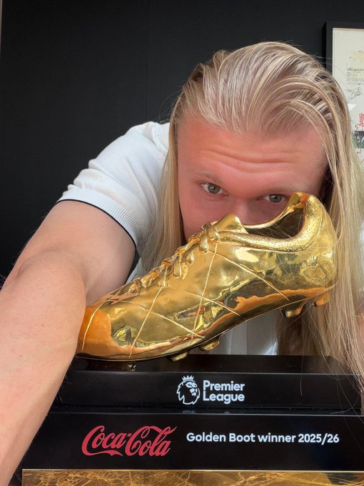 The image features a man leaning over a golden shoe with a plaque reading "Premier League" above it. The man appears to be posing for a photo while holding the shoe up to his face. The caption of the image reads, "What is Tria and why is it called a self custodial neobank? Many crypto projects talk about the future of money, but @useTria is focused on making crypto actually usable in everyday life today". This suggests that the golden shoe could be related to a coin or token created by Tria, which might have been used as an investment or for other purposes. The man's pose with the shoe and the plaque reading "Premier League" indicate that this golden shoe has some significance or connection to the Premier League sports team.