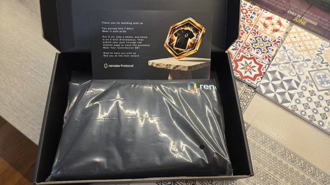 An open black box labeled 'renalis Protocol' containing a black pouch and a card that reads 'Thank you for building with us' and provides instructions for an 'Explorer Pass', sitting on a patterned tile floor.