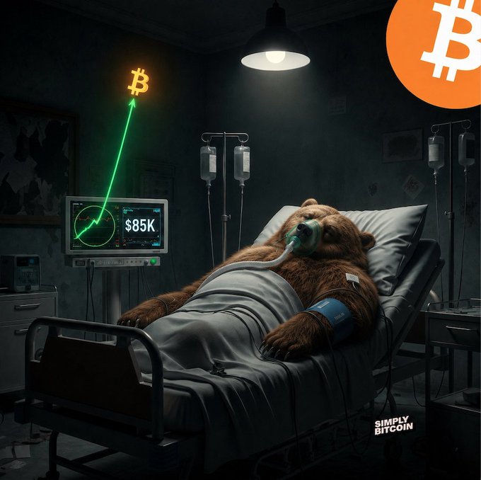 'Simply Bitcoin' illustration showing a bear on life support in a hospital bed while a Bitcoin price chart displays $85K with an upward green arrow.
