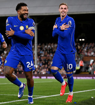 Two Chelsea soccer players, including #10, celebrate a goal on the pitch while wearing blue Chelsea kits.