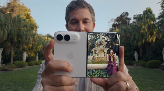 A man outdoors holds a foldable smartphone displaying a photo of a woman near a fountain, showcasing the device's screen.
