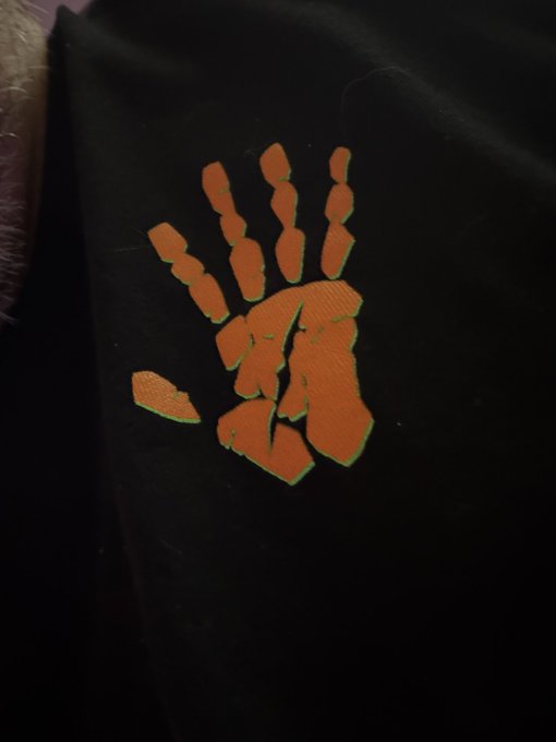 A close-up of a black fabric featuring an orange and green skeletal/zombie hand graphic with visible stitching details.