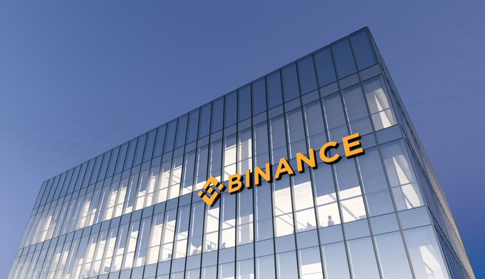 A modern glass office building displays the "BINANCE" logo and name in gold lettering against its reflective facade under a clear blue sky, symbolizing the cryptocurrency exchange's corporate expansion toward becoming a comprehensive financial "super app."