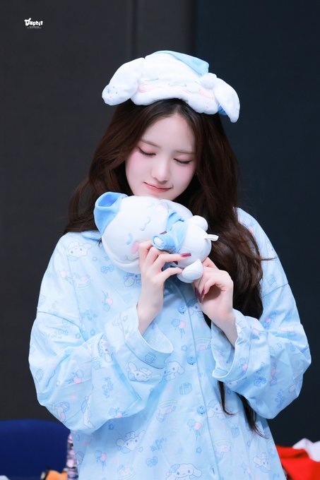 A young woman in a light blue pajama set with a matching headband holds a small blue plush toy close to her face, smiling gently. The text 'theqoo' is visible in the upper left corner.
