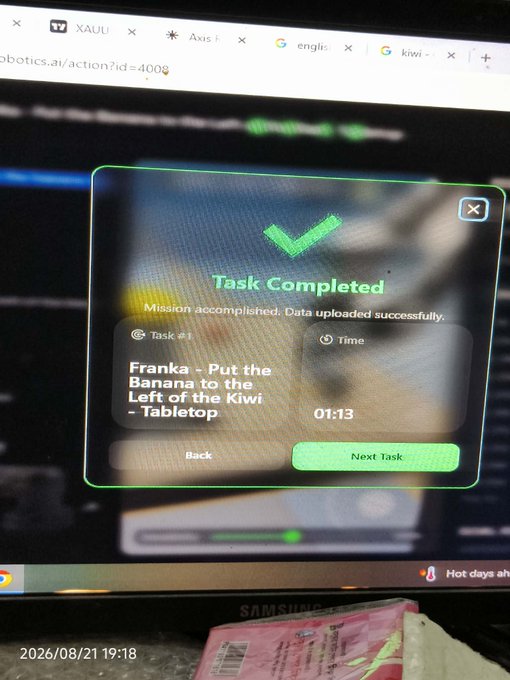 A computer screen showing a 'Task Completed' confirmation popup for 'Franka - Put the Banana to the Left of the Kiwi - Tabletop' completed in 01:13, with browser tabs visible including 'XAUU' and 'Axis'.